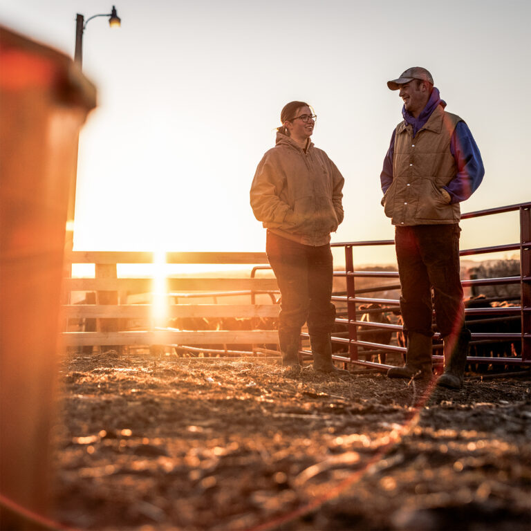 two ranchers stand outside with a sunrise